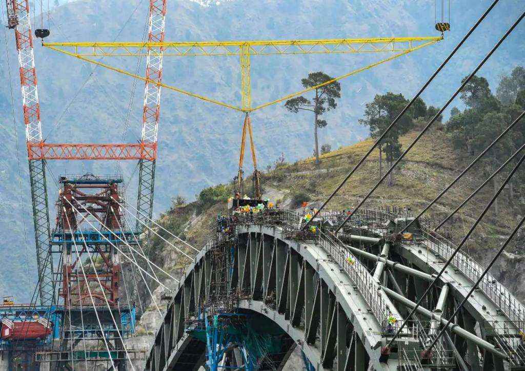 Workers building the Chenab Bridge using cable cranes across a deep valley in challenging Himalayan terrain